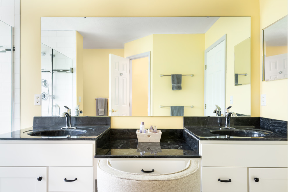 This is an example of a medium sized traditional ensuite bathroom in Cincinnati with shaker cabinets, white cabinets, a walk-in shower, a two-piece toilet, white tiles, metro tiles, yellow walls, laminate floors, an integrated sink, marble worktops, grey floors, a hinged door and black worktops.