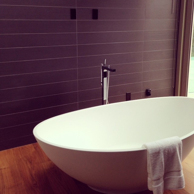 Diseño de cuarto de baño principal contemporáneo de tamaño medio con bañera exenta, baldosas y/o azulejos negros, suelo de madera en tonos medios y paredes púrpuras