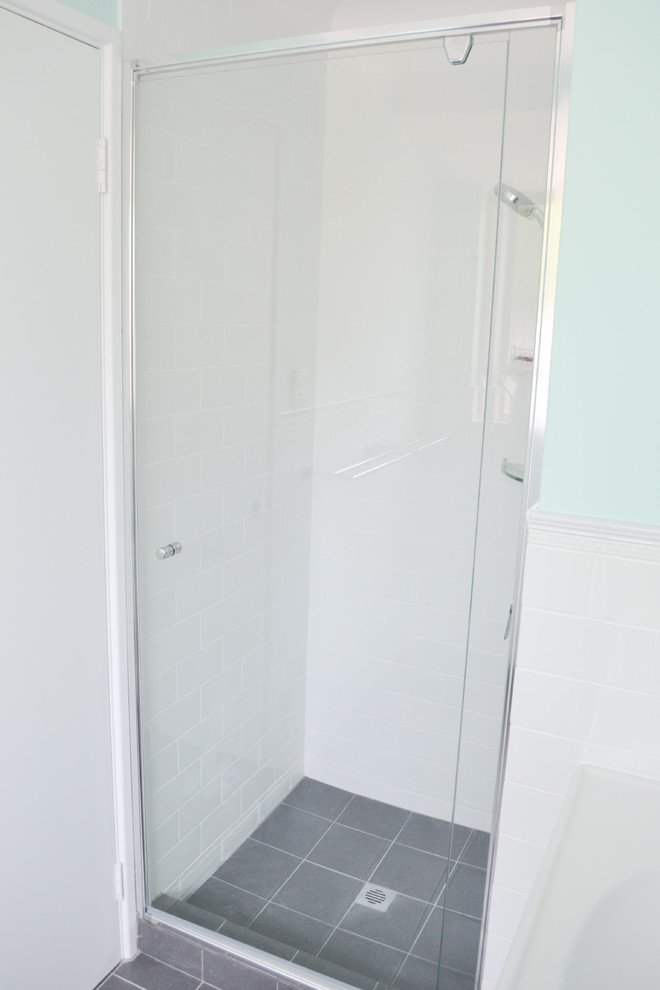 Inredning av ett litet en-suite badrum, med vita skåp, en dusch i en alkov, en toalettstol med hel cisternkåpa, vit kakel, vita väggar, klinkergolv i keramik, ett integrerad handfat, bänkskiva i akrylsten, grått golv och dusch med gångjärnsdörr
