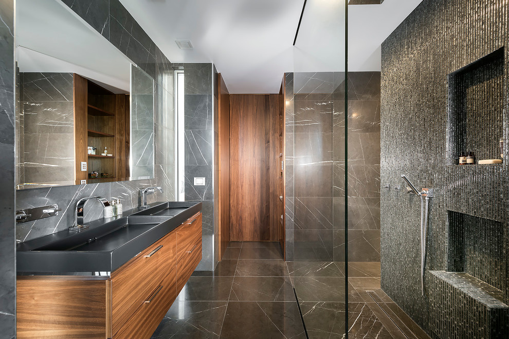 Cette image montre une salle de bain design en bois foncé avec un placard à porte plane, un carrelage gris, un lavabo intégré, une douche ouverte et aucune cabine.