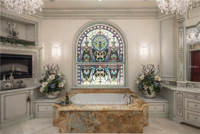 Expansive traditional ensuite bathroom in Orlando with freestanding cabinets, grey cabinets, a built-in bath, a walk-in shower, a two-piece toilet, white tiles, stone slabs, white walls, marble flooring, a submerged sink and onyx worktops.