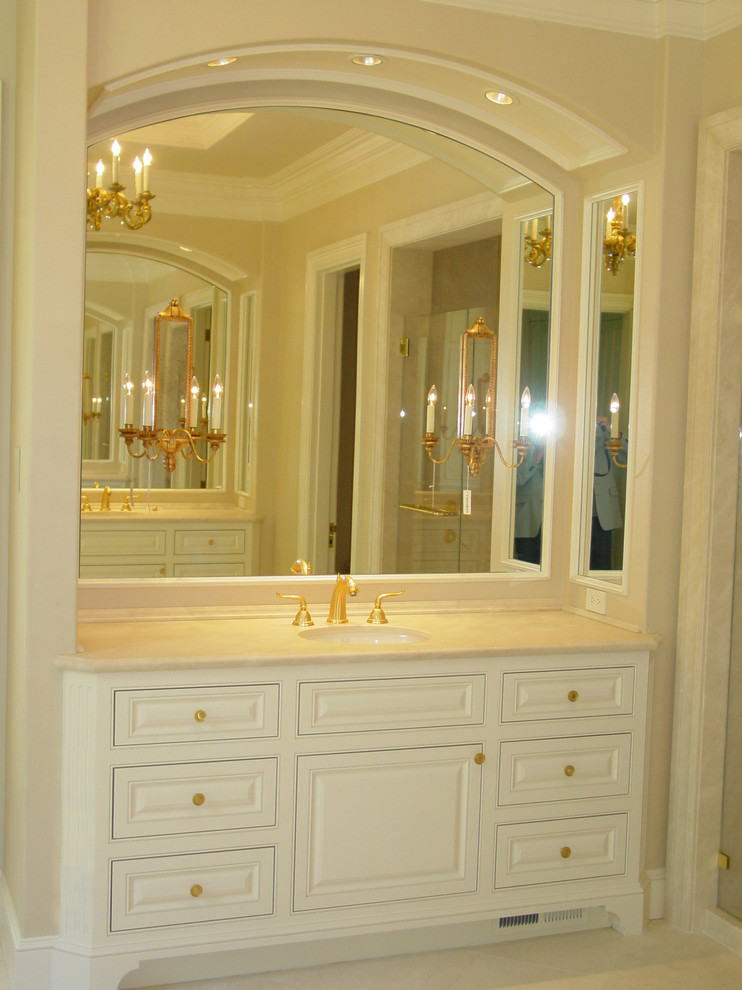 Modelo de cuarto de baño principal clásico con lavabo bajoencimera, armarios con rebordes decorativos, puertas de armario blancas y encimera de mármol
