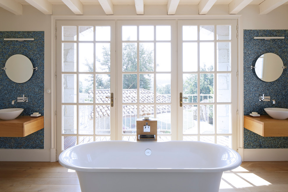 Réalisation d'une grande salle de bain principale champêtre en bois clair avec une vasque, un placard sans porte, un plan de toilette en bois, une baignoire indépendante, un carrelage bleu, mosaïque et parquet clair.
