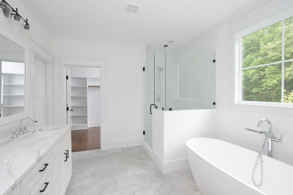 This is an example of a large classic ensuite bathroom in Raleigh with shaker cabinets, white cabinets, a freestanding bath, an alcove shower, a two-piece toilet, white tiles, ceramic tiles, white walls, ceramic flooring, a submerged sink, engineered stone worktops, grey floors, a hinged door, multi-coloured worktops, an enclosed toilet and double sinks.