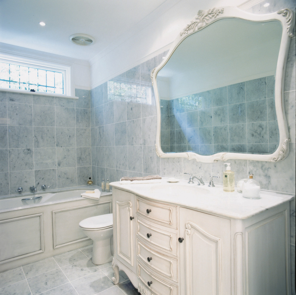 Свежая идея для дизайна: ванная комната среднего размера в классическом стиле с белыми фасадами, полновстраиваемой ванной, раздельным унитазом, серой плиткой, серыми стенами, врезной раковиной, мраморной столешницей и серым полом - отличное фото интерьера