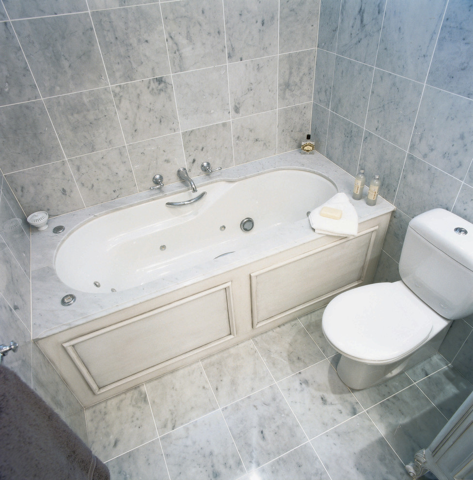 Klassisk inredning av ett mellanstort badrum, med ett undermonterat badkar, en toalettstol med separat cisternkåpa, grå kakel, grå väggar och grått golv