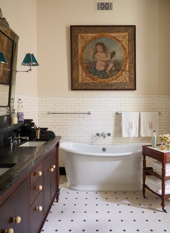 На фото: ванная комната в классическом стиле с темными деревянными фасадами, отдельно стоящей ванной, белой плиткой, плиткой кабанчик, бежевыми стенами, полом из мозаичной плитки, врезной раковиной, разноцветным полом, черной столешницей и плоскими фасадами с