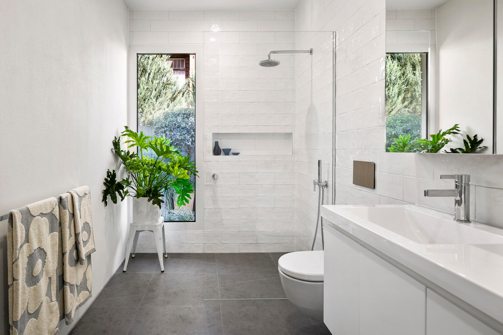 Exempel på ett stort modernt gul gult badrum med dusch, med släta luckor, vita skåp, en öppen dusch, en vägghängd toalettstol, vit kakel, keramikplattor, vita väggar, klinkergolv i porslin, ett integrerad handfat, grått golv och med dusch som är öppen
