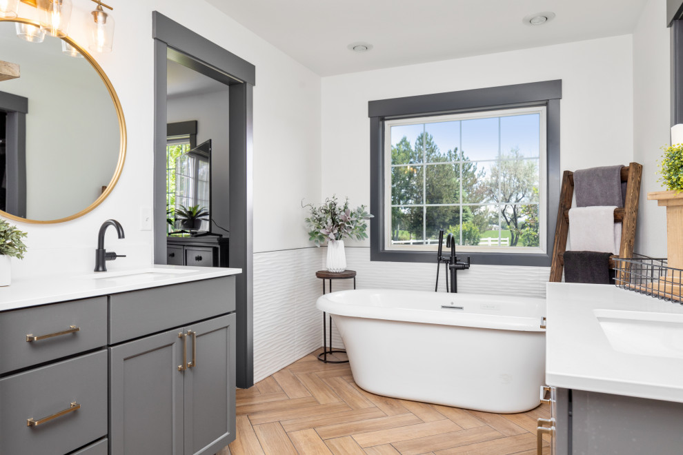 Foto på ett lantligt vit badrum, med skåp i shakerstil, grå skåp, ett fristående badkar, vita väggar, ett undermonterad handfat och brunt golv
