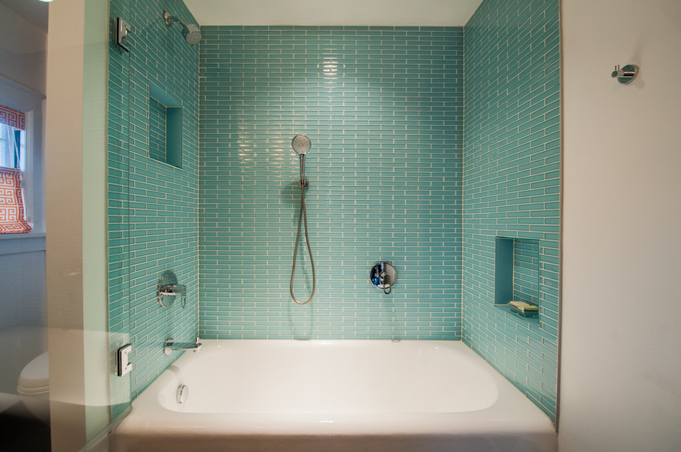 Inredning av ett klassiskt mellanstort badrum, med ett undermonterad handfat, släta luckor, skåp i mellenmörkt trä, bänkskiva i kvarts, ett badkar i en alkov, en dusch/badkar-kombination, en toalettstol med separat cisternkåpa, blå kakel, glaskakel, vita väggar och klinkergolv i porslin