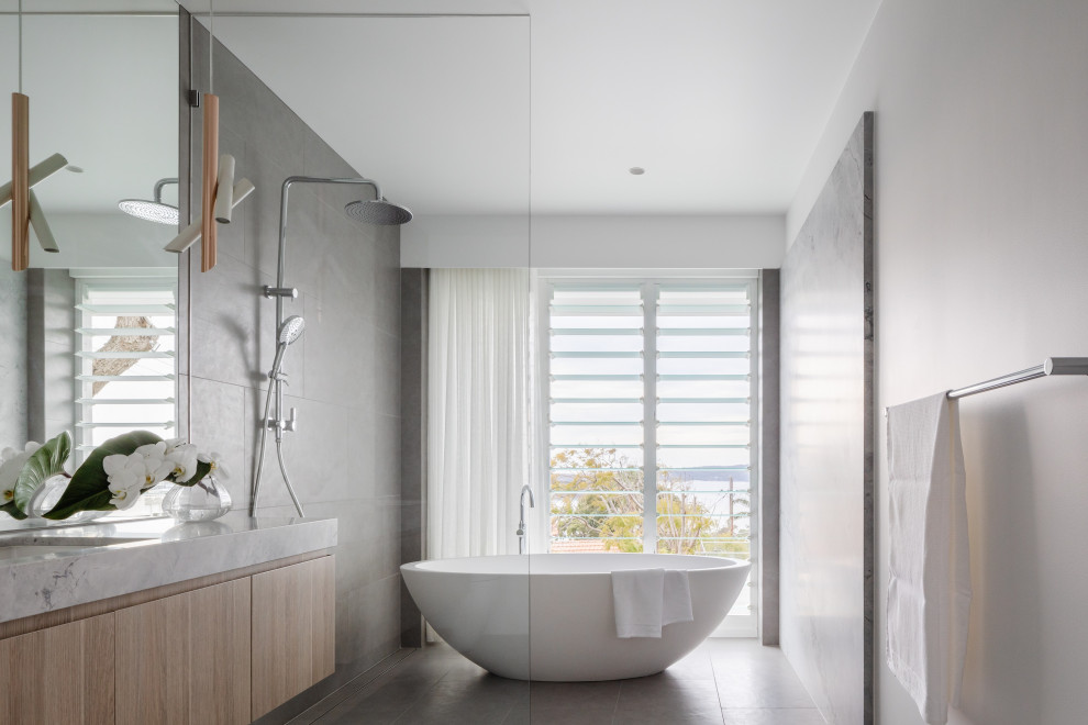 Idéer för stora funkis grått badrum, med ett fristående badkar, granitbänkskiva, släta luckor, skåp i ljust trä, våtrum, grå kakel, vita väggar, ett undermonterad handfat och grått golv