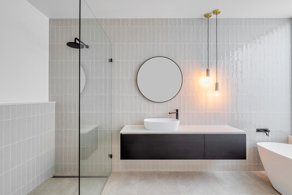 Idéer för att renovera ett funkis vit vitt badrum, med släta luckor, svarta skåp, ett fristående badkar, en kantlös dusch, grå kakel, vita väggar, ett fristående handfat, grått golv och med dusch som är öppen