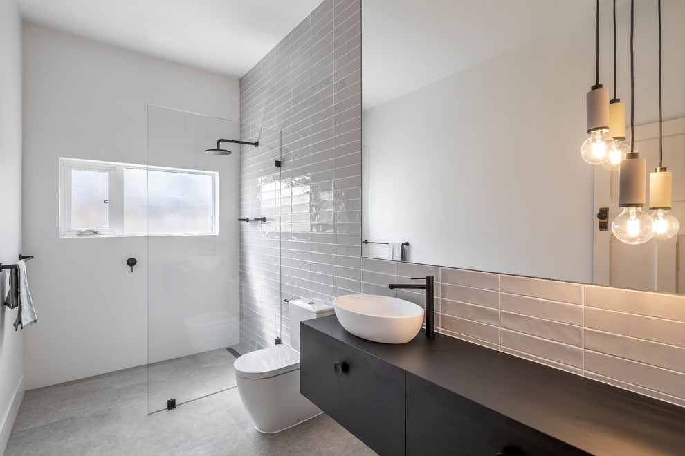 Inspiration för ett funkis svart svart badrum med dusch, med släta luckor, svarta skåp, en kantlös dusch, grå kakel, vita väggar, ett fristående handfat, träbänkskiva, grått golv och med dusch som är öppen