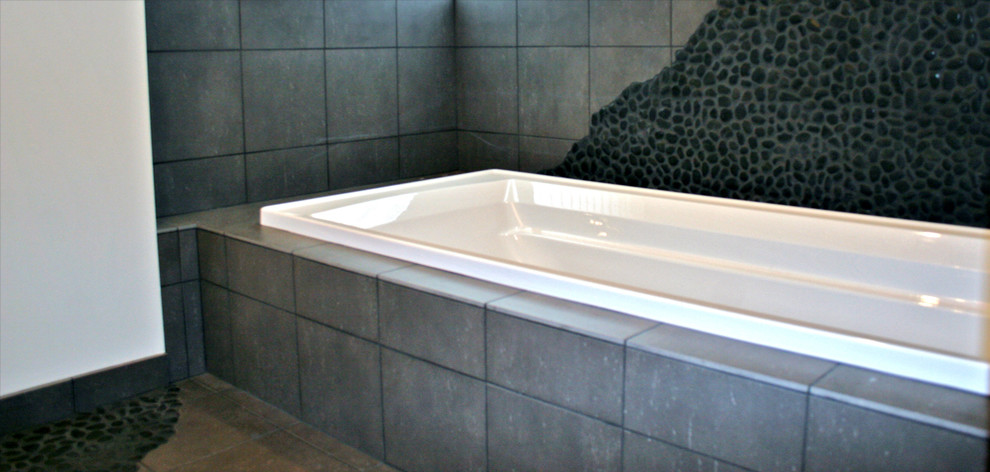 Modelo de cuarto de baño principal minimalista con bañera encastrada, combinación de ducha y bañera, baldosas y/o azulejos grises, suelo de baldosas tipo guijarro, suelo de baldosas tipo guijarro y suelo negro