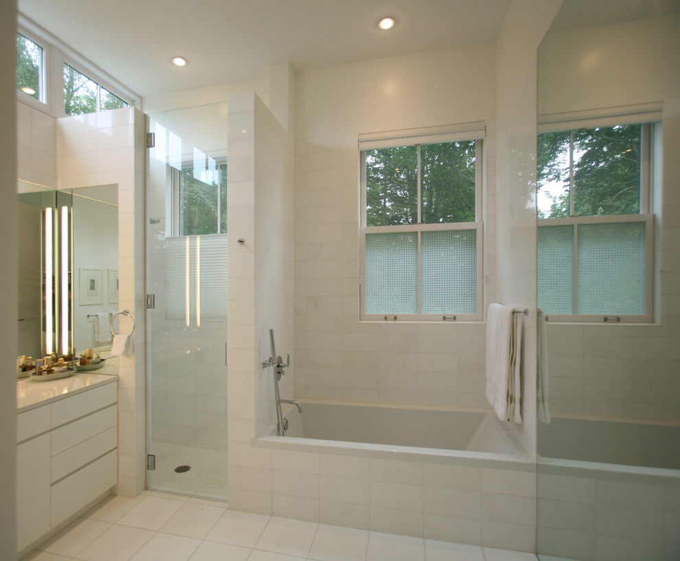 Klassisk inredning av ett badrum, med släta luckor, vita skåp, ett badkar i en alkov, en dusch i en alkov och vit kakel
