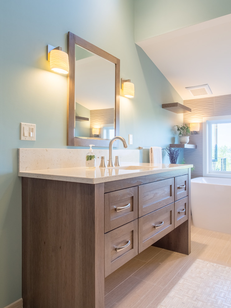 Example of a mid-sized transitional master beige tile and porcelain tile porcelain tile, beige floor, double-sink and vaulted ceiling bathroom design in Seattle with recessed-panel cabinets, medium tone wood cabinets, a two-piece toilet, blue walls, an undermount sink, quartz countertops, a hinged shower door, beige countertops, a freestanding vanity and a niche