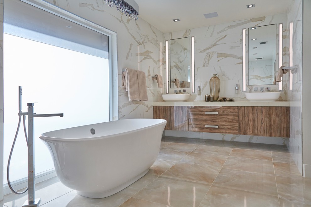 Bild på ett mellanstort funkis en-suite badrum, med släta luckor, bruna skåp, ett fristående badkar, vit kakel, ett fristående handfat, beiget golv, marmorkakel, bruna väggar och marmorgolv