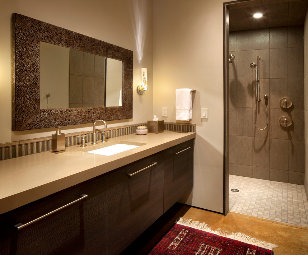 Пример оригинального дизайна: большая ванная комната в современном стиле с плоскими фасадами, темными деревянными фасадами, открытым душем, коричневой плиткой, керамогранитной плиткой, бежевыми стенами, бетонным полом, врезной раковиной и столешницей из искусственного кварца