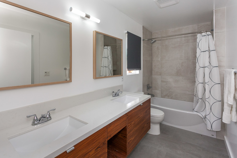 Bild på ett mellanstort vintage grå grått en-suite badrum, med släta luckor, skåp i mellenmörkt trä, ett badkar i en alkov, en dusch/badkar-kombination, en toalettstol med separat cisternkåpa, beige kakel, porslinskakel, vita väggar, ett undermonterad handfat, bänkskiva i kvartsit, ljust trägolv, grått golv och dusch med duschdraperi