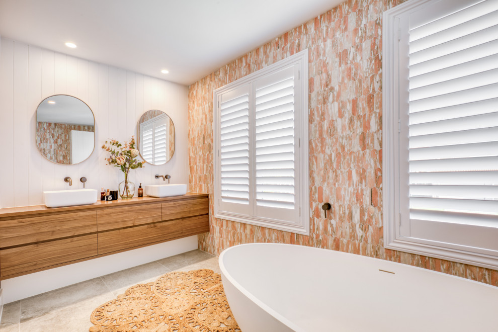 Klassisk inredning av ett brun brunt en-suite badrum, med släta luckor, skåp i mellenmörkt trä, ett fristående badkar, vit kakel, ett fristående handfat, träbänkskiva och beiget golv