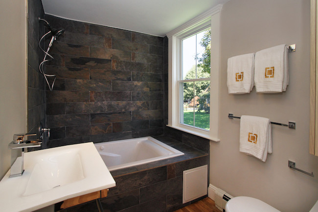 Bild på ett mellanstort funkis en-suite badrum, med släta luckor, ett platsbyggt badkar, en toalettstol med hel cisternkåpa, svart kakel, porslinskakel, beige väggar, ljust trägolv och ett nedsänkt handfat