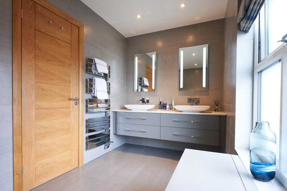 This is an example of a medium sized contemporary ensuite bathroom in Other with flat-panel cabinets, grey cabinets, an alcove shower, a wall mounted toilet, grey tiles, a vessel sink, quartz worktops, an open shower, a freestanding bath, white walls and vinyl flooring.