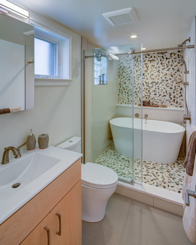 На фото: главная ванная комната среднего размера в современном стиле с плоскими фасадами, светлыми деревянными фасадами, отдельно стоящей ванной, душевой комнатой, унитазом-моноблоком, разноцветной плиткой, галечной плиткой, белыми стенами, полом из галечной плитки, монолитной раковиной, столешницей из искусственного камня, разноцветным полом, душем с раздвижными дверями и белой столешницей