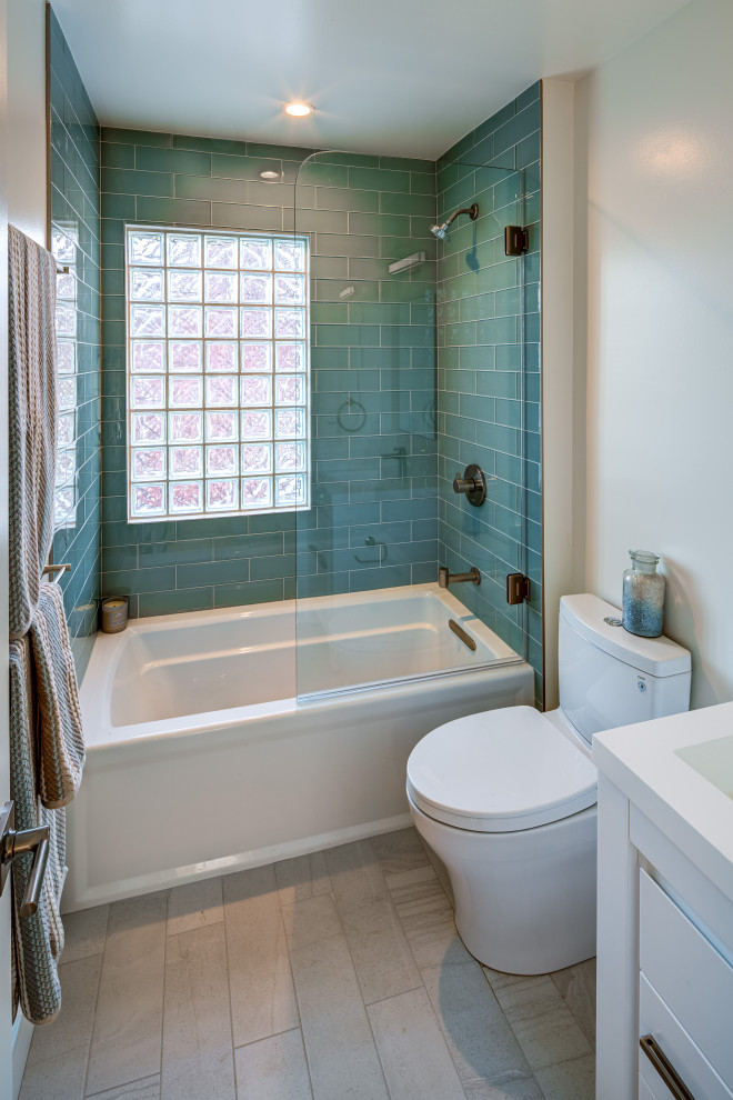Exemple d'une salle de bain chic en bois clair de taille moyenne pour enfant avec un placard à porte plane, une baignoire indépendante, un combiné douche/baignoire, WC à poser, un carrelage bleu, un carrelage en pâte de verre, un mur blanc, un sol en carrelage de céramique, un lavabo intégré, un plan de toilette en surface solide, un sol beige, une cabine de douche à porte battante et un plan de toilette blanc.