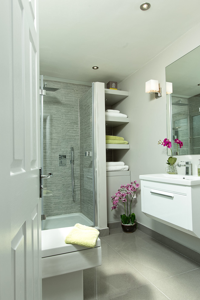 Cette image montre une salle d'eau traditionnelle avec un placard à porte plane, des portes de placard blanches, une douche d'angle, un carrelage gris, un mur gris et un plan vasque.
