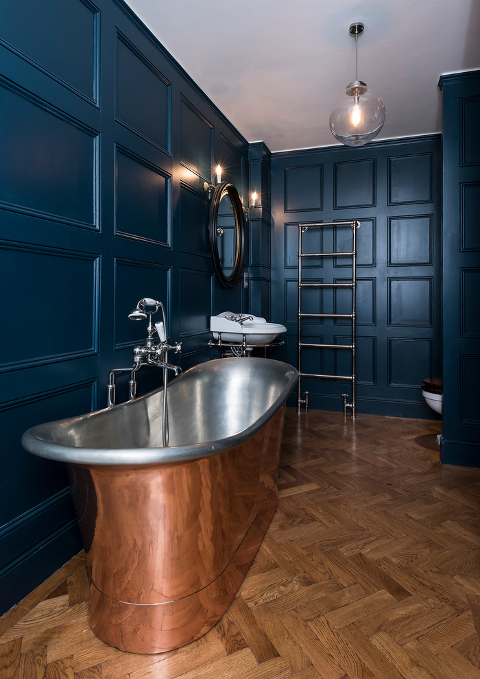 Réalisation d'une grande salle de bain principale tradition avec un lavabo suspendu, une baignoire indépendante, un combiné douche/baignoire, WC à poser, un mur bleu et parquet clair.