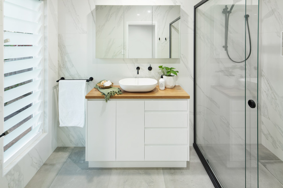 This is an example of a beach style bathroom in Sunshine Coast with white cabinets, a walk-in shower, black and white tiles, porcelain tiles, white walls, cement flooring, wooden worktops, grey floors and a sliding door.