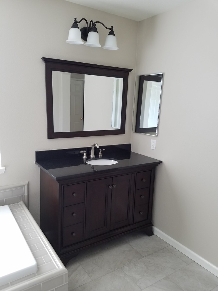 Medium sized contemporary ensuite bathroom in Los Angeles with freestanding cabinets, brown cabinets, a built-in bath, a corner shower, a two-piece toilet, beige walls, porcelain flooring, a submerged sink, engineered stone worktops, beige floors, a hinged door and black worktops.