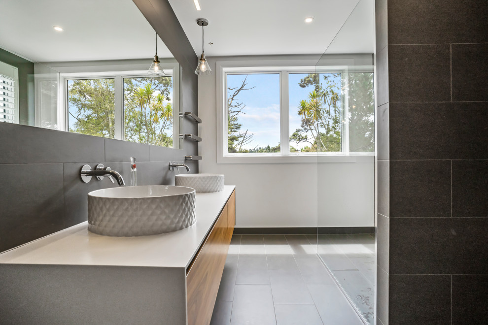 Modern inredning av ett mycket stort grå grått en-suite badrum, med en kantlös dusch, grå kakel, cementgolv, grått golv, med dusch som är öppen, släta luckor, skåp i mellenmörkt trä, vita väggar och ett fristående handfat