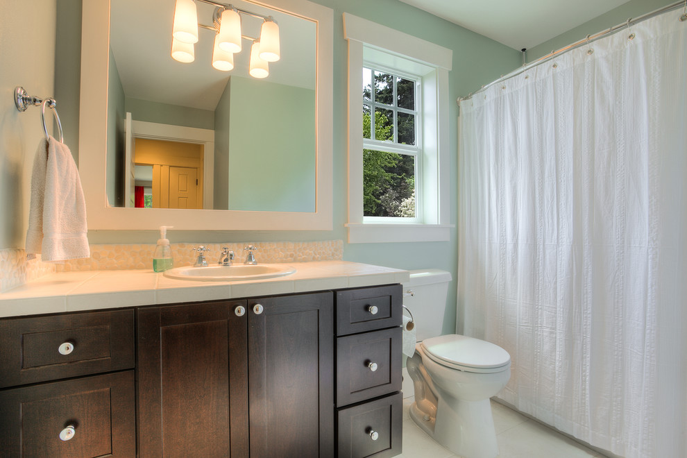 Пример оригинального дизайна: детская ванная комната среднего размера в стиле кантри с фасадами в стиле шейкер, темными деревянными фасадами, душем над ванной, унитазом-моноблоком, белой плиткой, синими стенами, полом из керамогранита, накладной раковиной и столешницей из плитки