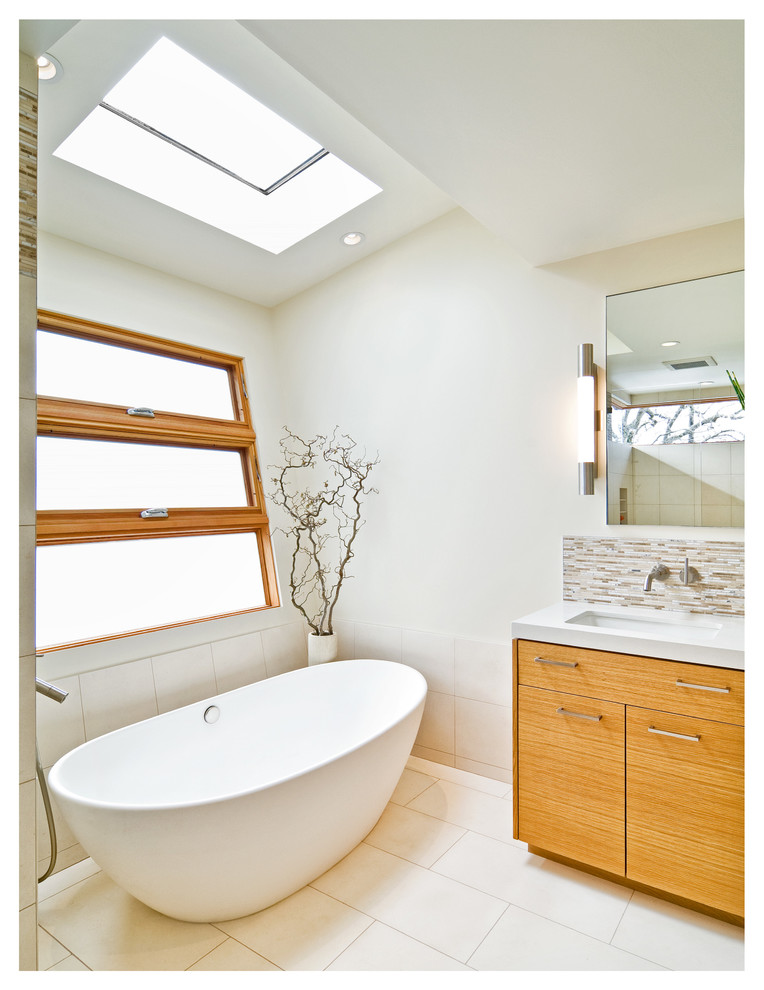 Стильный дизайн: главная ванная комната среднего размера в стиле модернизм с накладной раковиной, плоскими фасадами, светлыми деревянными фасадами, отдельно стоящей ванной, раздельным унитазом, разноцветной плиткой, белыми стенами, полом из керамогранита и бежевым полом - последний тренд