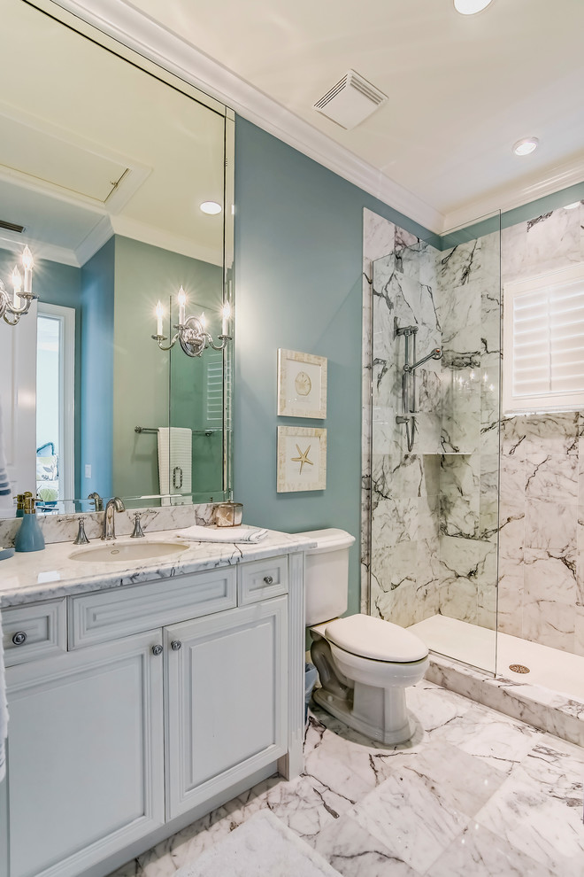 Klassisk inredning av ett mellanstort badrum med dusch, med ett nedsänkt handfat, luckor med upphöjd panel, vita skåp, marmorbänkskiva, en öppen dusch, en toalettstol med separat cisternkåpa, vit kakel, stenhäll, blå väggar och marmorgolv