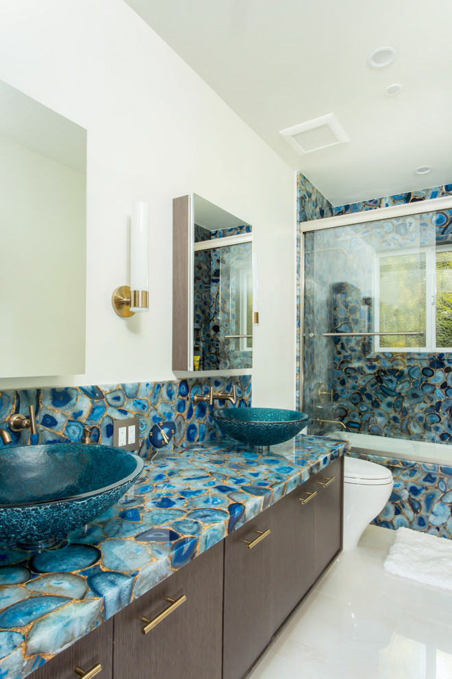 Design ideas for a medium sized bohemian family bathroom in Los Angeles with flat-panel cabinets, dark wood cabinets, a built-in bath, a shower/bath combination, a one-piece toilet, blue tiles, stone slabs, white walls, porcelain flooring, a vessel sink, white floors and a sliding door.