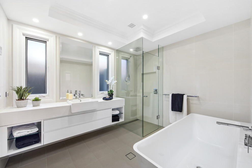 Cette image montre une salle de bain principale design avec un placard à porte plane, des portes de placard blanches, une baignoire indépendante, une douche d'angle, un carrelage gris, un mur gris, un lavabo posé, un sol gris, une cabine de douche à porte battante et un plan de toilette blanc.