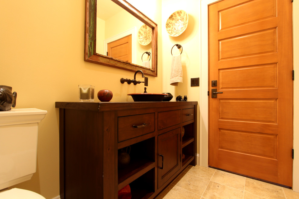 Lantlig inredning av ett mellanstort badrum, med möbel-liknande, en toalettstol med separat cisternkåpa, beige kakel, stenkakel, gula väggar, travertin golv, ett fristående handfat, träbänkskiva och skåp i mellenmörkt trä