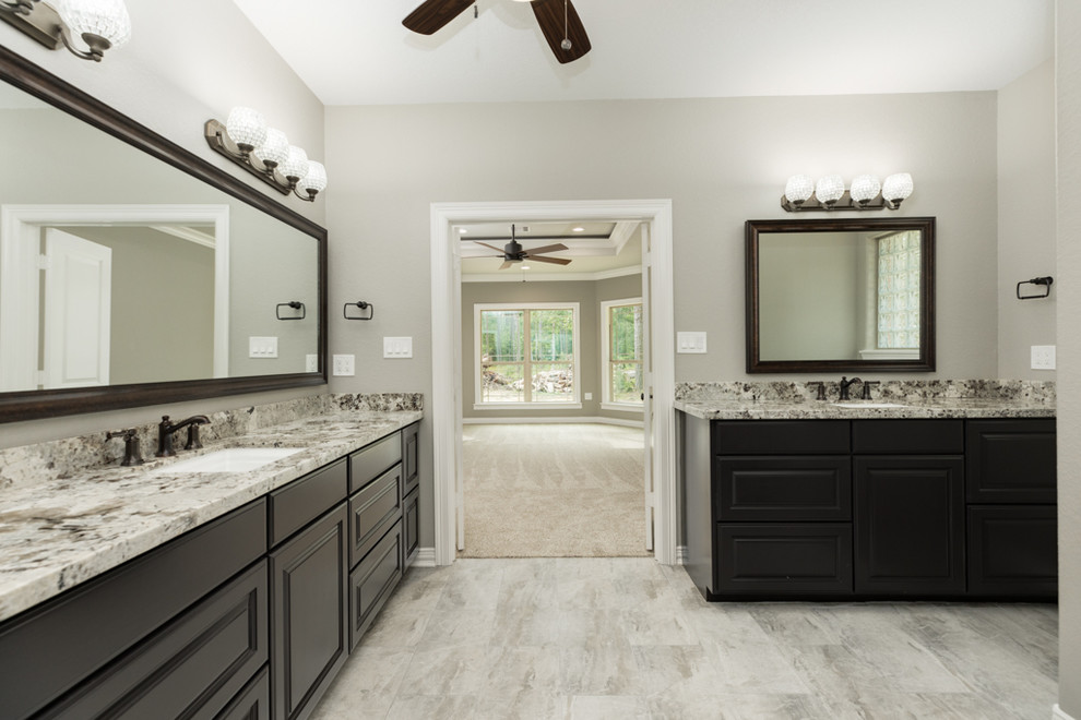 Expansive classic ensuite bathroom in Houston with raised-panel cabinets, brown cabinets, a walk-in shower, a two-piece toilet, beige tiles, mirror tiles, beige walls, porcelain flooring, a submerged sink, granite worktops, grey floors and an open shower.