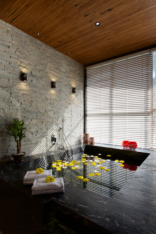 Exemple d'une salle de bain principale asiatique avec un bain bouillonnant, un carrelage de pierre et un sol noir.