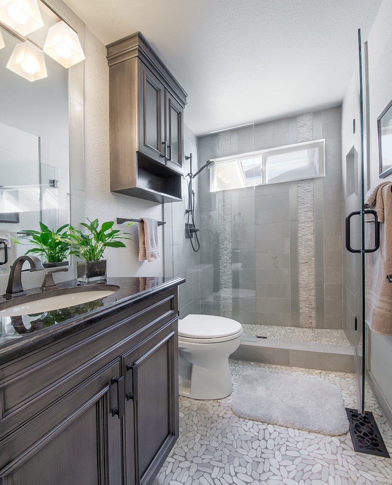 Photo of a medium sized traditional ensuite bathroom in Denver with a built-in sink, beaded cabinets, dark wood cabinets, a corner shower, a one-piece toilet, grey tiles, white walls and pebble tile flooring.