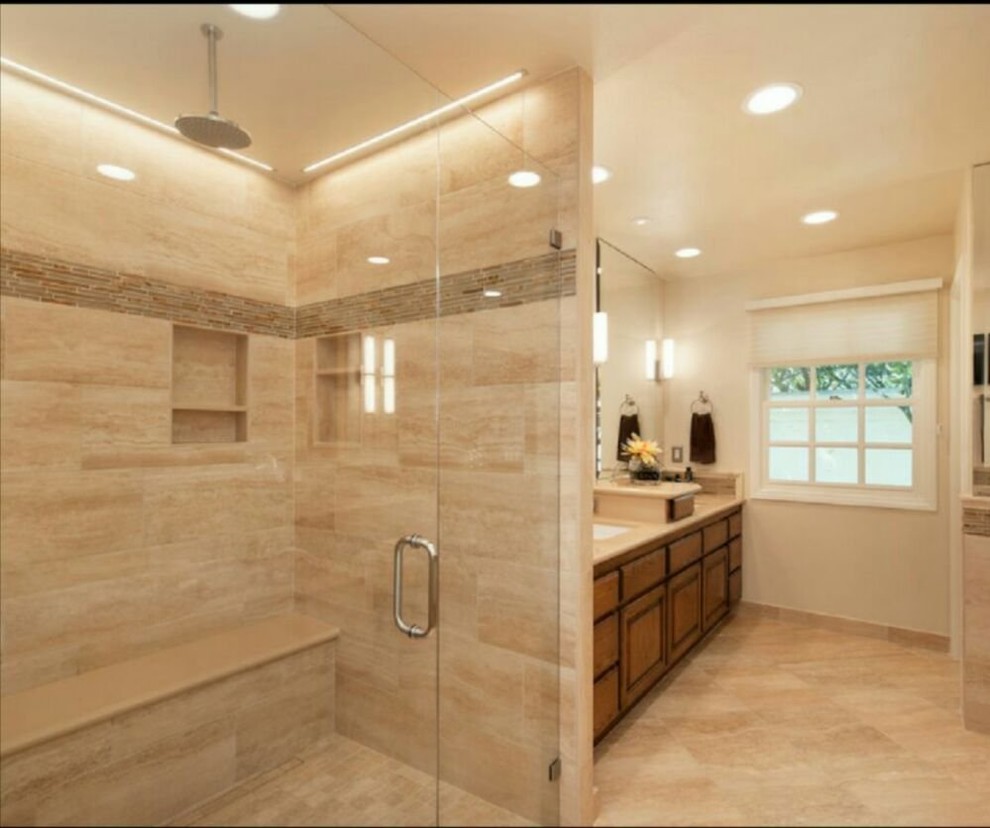 Cette image montre une grande salle de bain principale traditionnelle en bois brun avec un placard avec porte à panneau surélevé, un espace douche bain, un carrelage beige, du carrelage en travertin, un mur beige, un sol en travertin, un lavabo encastré et un plan de toilette en calcaire.