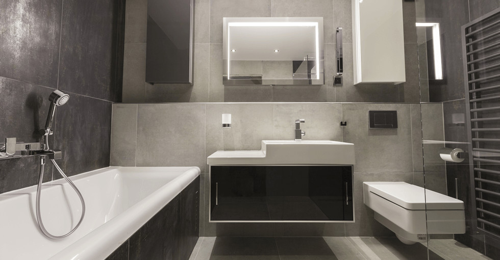 Modern inredning av ett mellanstort badrum med dusch, med släta luckor, svarta skåp, ett badkar i en alkov, en toalettstol med hel cisternkåpa, vit kakel, grå väggar, skiffergolv, ett avlångt handfat, kaklad bänkskiva och grått golv