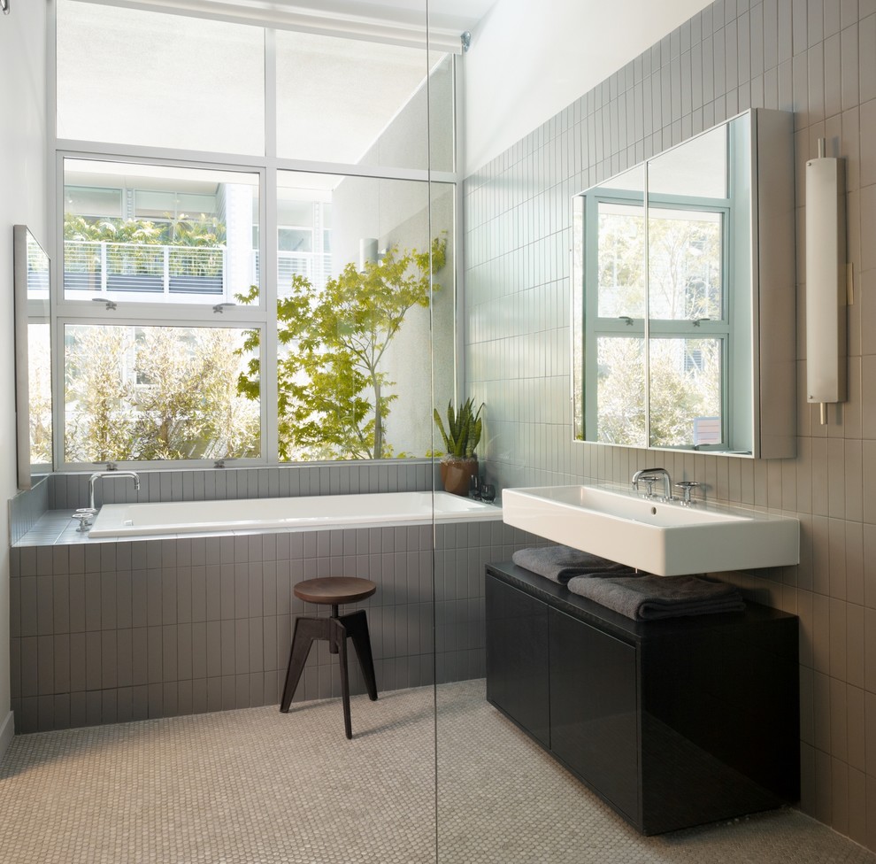 Diseño de cuarto de baño urbano con lavabo suspendido, armarios con paneles lisos, puertas de armario negras, bañera encastrada y baldosas y/o azulejos grises