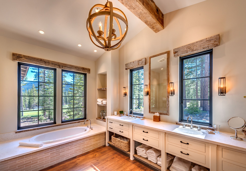 Medium sized rustic ensuite bathroom in Sacramento with beige walls, flat-panel cabinets, beige cabinets, medium hardwood flooring, a submerged sink, engineered stone worktops, beige floors, a built-in bath, an alcove shower, beige tiles, porcelain tiles and a hinged door.