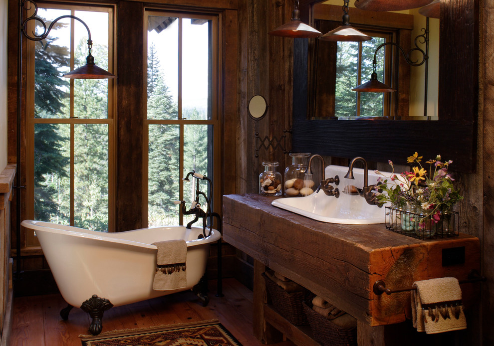 Cette photo montre une petite salle d'eau montagne en bois brun avec un placard sans porte, une baignoire sur pieds, un mur marron, un sol en bois brun, une grande vasque, un plan de toilette en bois, un sol marron et un plan de toilette marron.