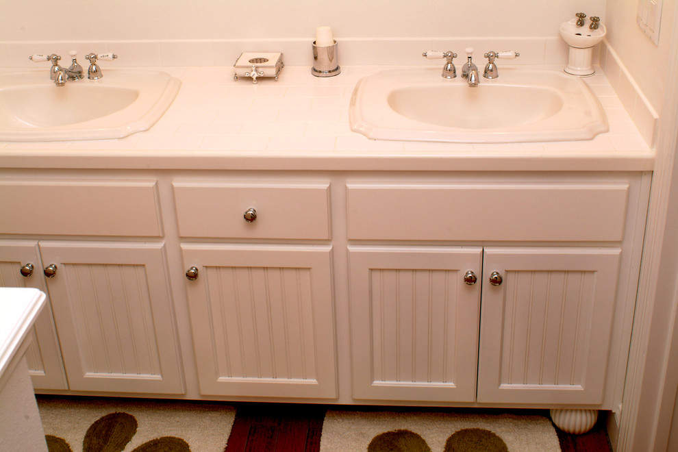 Bild på ett mellanstort vintage badrum med dusch, med luckor med infälld panel, vita skåp, ett badkar i en alkov, en dusch/badkar-kombination, en toalettstol med separat cisternkåpa, vit kakel, keramikplattor, beige väggar, mellanmörkt trägolv, ett nedsänkt handfat, kaklad bänkskiva, brunt golv och dusch med duschdraperi