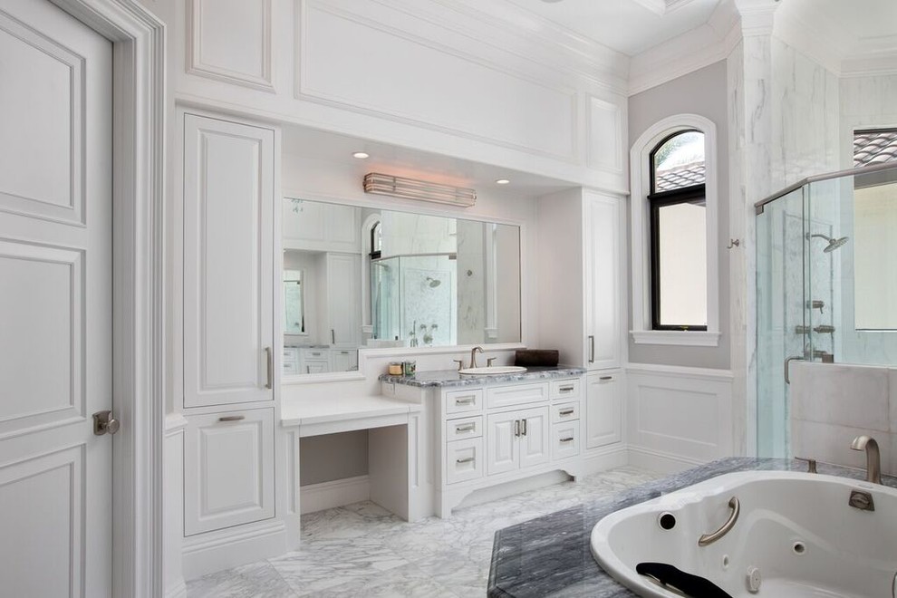 Expansive traditional ensuite bathroom in Miami with raised-panel cabinets, white cabinets, a built-in bath, an alcove shower, grey tiles, stone tiles, grey walls, a built-in sink, marble flooring, marble worktops, grey floors and a hinged door.