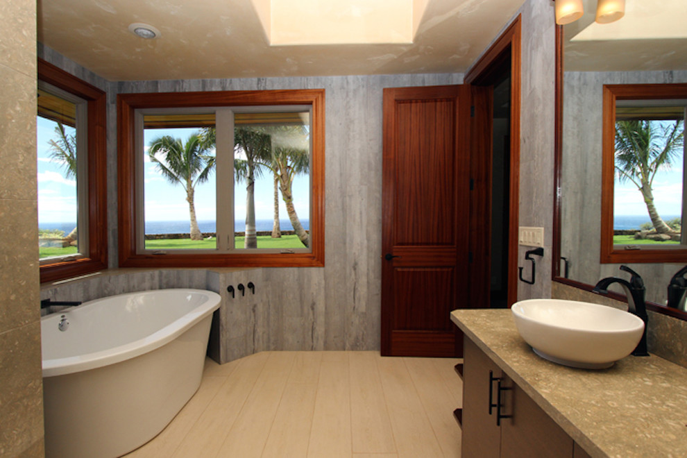 Exotisk inredning av ett badrum, med släta luckor, skåp i mörkt trä, ett fristående badkar, grå väggar och klinkergolv i porslin